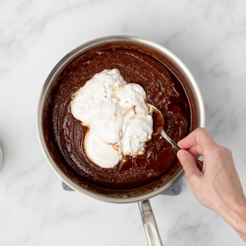 hand holding mixing spoon with white marshmallow cream in clumps on top