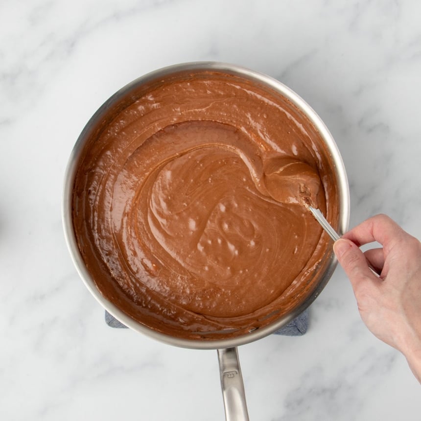 hand mixing light brown thick swirled mixture in pan, mixing in marshmallow cream