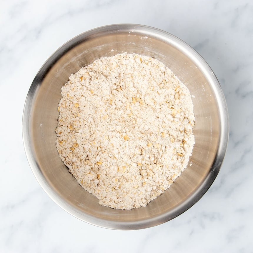 large round metal mixing bowl with light brown oats and oat flour mixed together