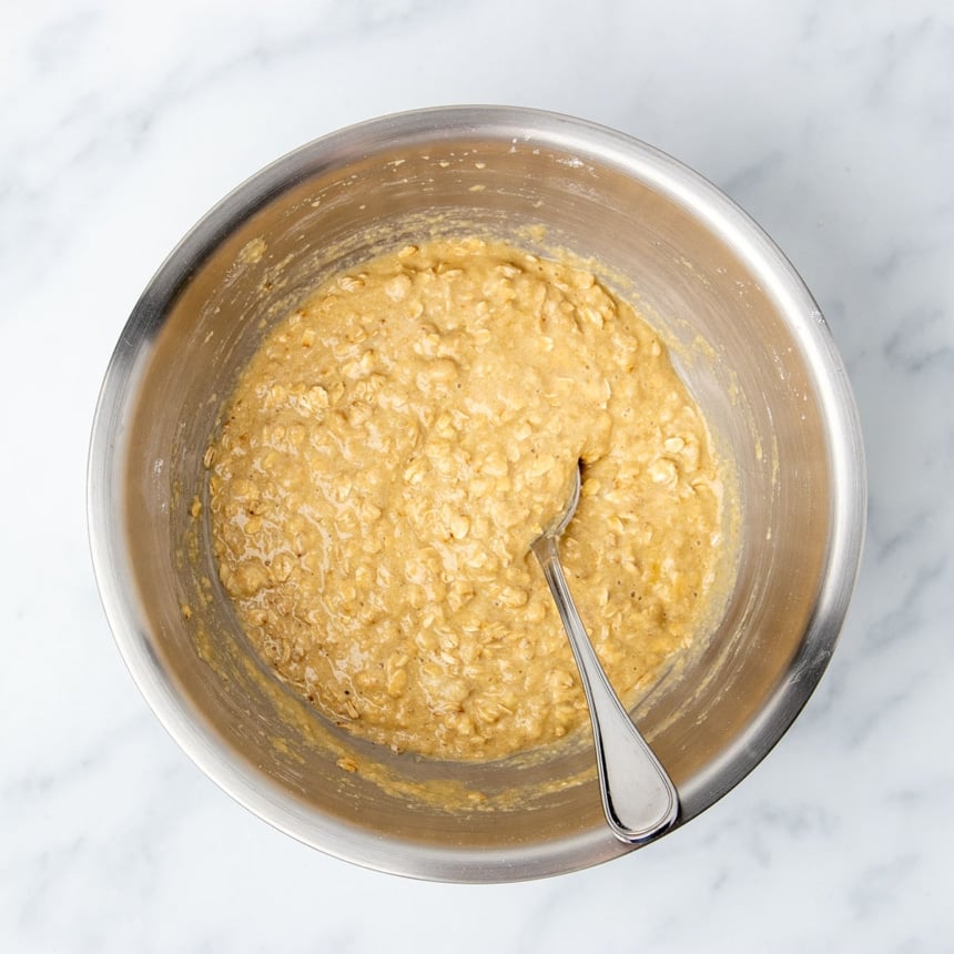 light brown raw breakfast cookie batter with wet and dry ingredients mixed together, with large metal mixing spoon