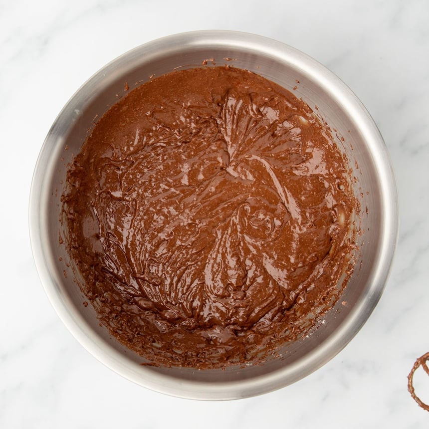 same bowl with thicker brown mixture after almond flour was beaten into Nutella and egg mixture, with one beater partially visible