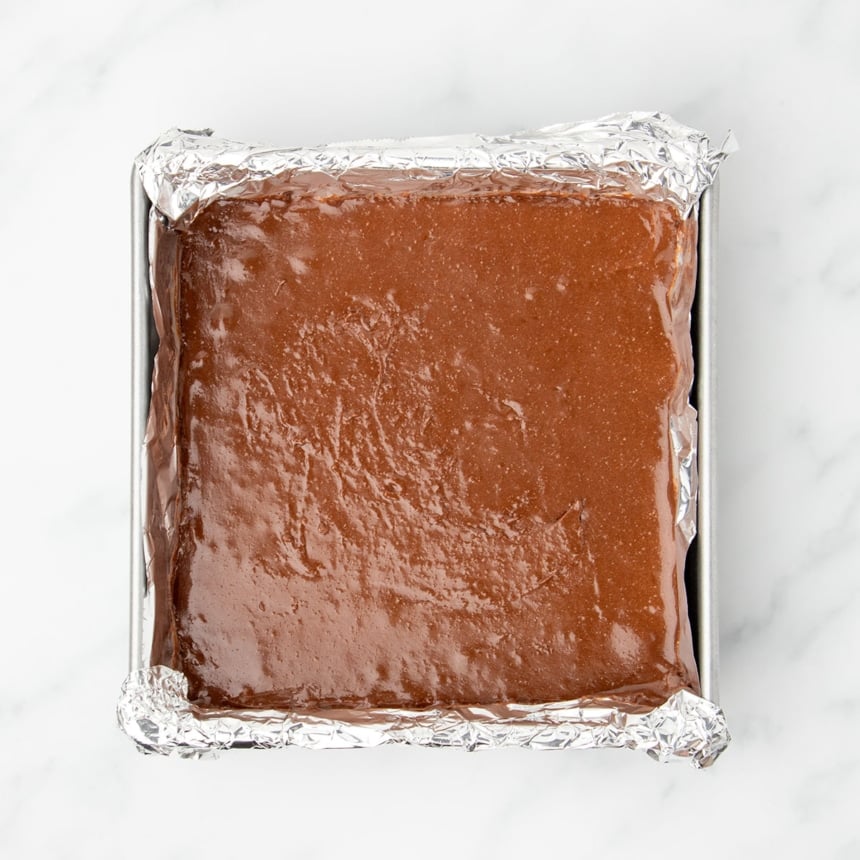 8-inch square metal baking pan lined with foil, with raw dark brown 3 ingredient brownie mixture in single layer in pan