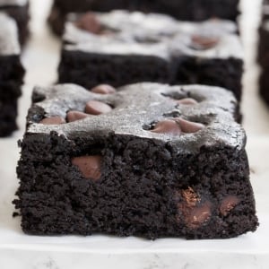 square very dark brown black bean brownies with visible lighter brown chocolate chips on white paper