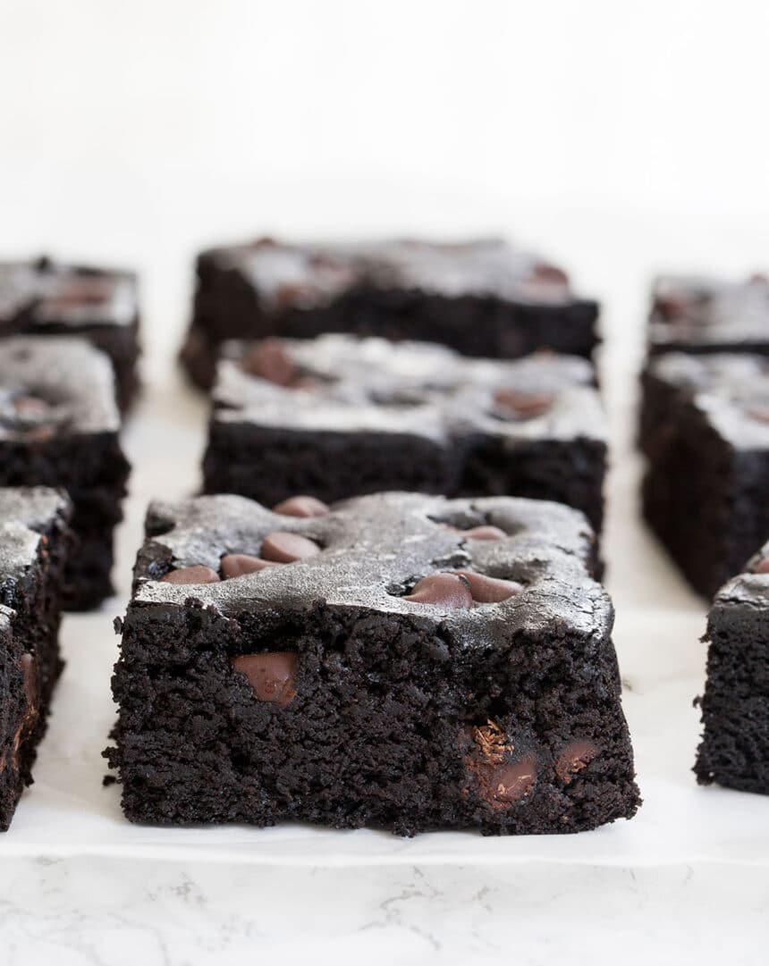 Side image of chocolate chip black bean brownie squares on white paper on marble countertop