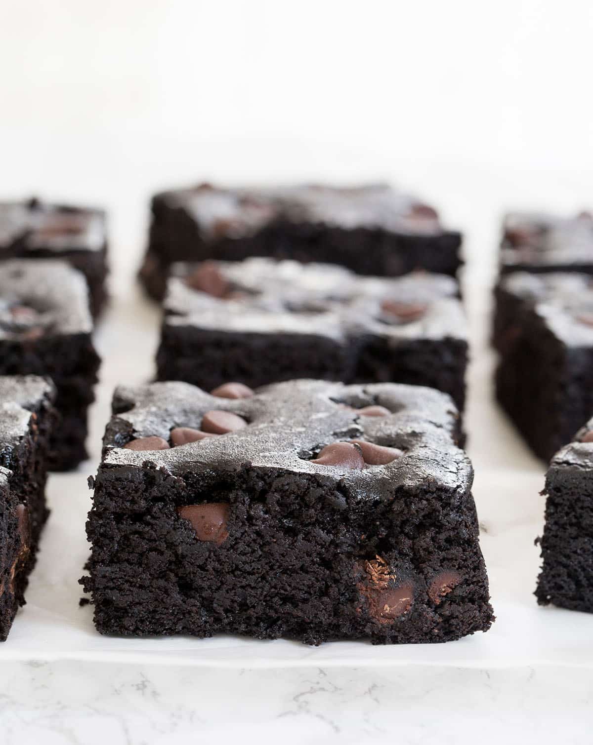 Side image of chocolate chip black bean brownie squares on white paper on marble countertop