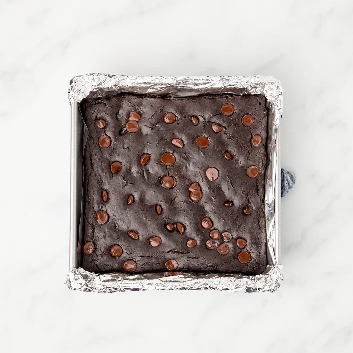 Same square baking pan with baked dark brownies with lighter brown melted chips on top.