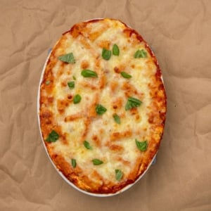 Gluten free baked ziti overhead image on brown paper with chopped fresh basil leaves on top