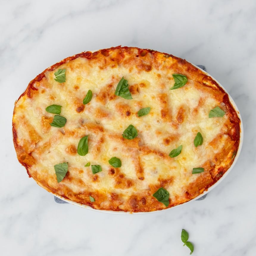 Finished baked ziti in casserole dish with browned spots on cheese and fresh chopped basil scattered on top