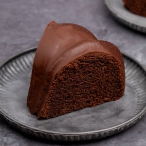 brown slice of gluten free chocolate bundt cake with hard chocolate icing on small gray fluted plate on gray surface