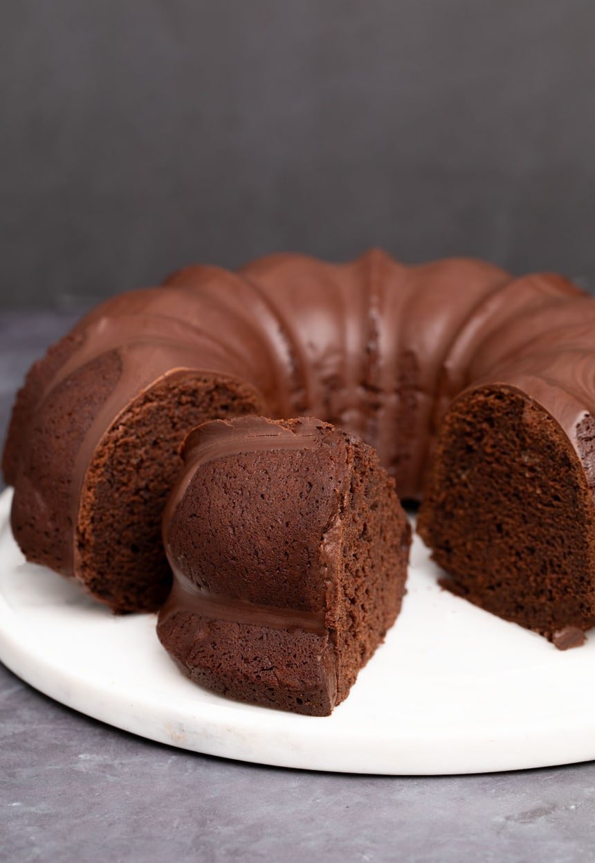 mostly whole round gluten free chocolate bundt cake with 2 slices cut, one missing and one on its side on round marble cake plate