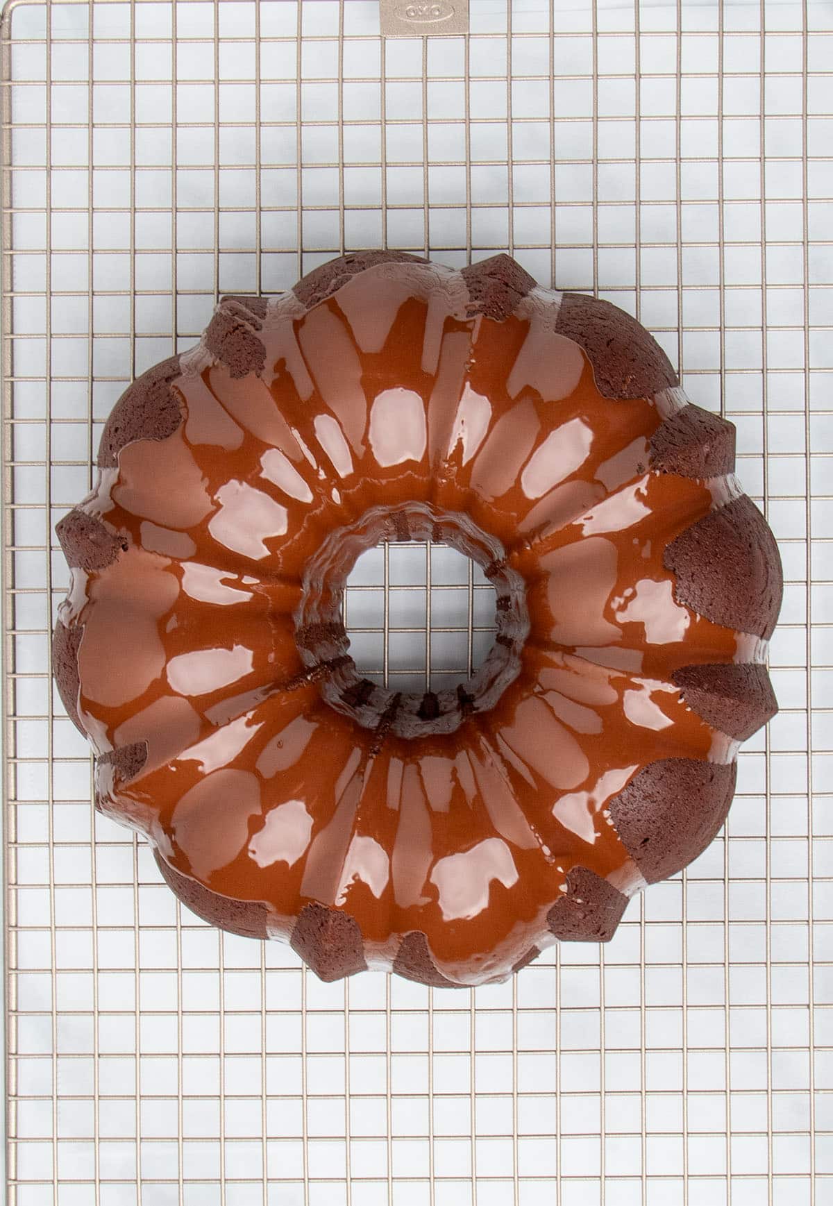 overhead image of fresh shiny brown chocolate glaze on dark brown chocolate bundt cake on gold colored wire rack
