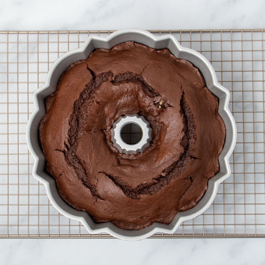 same pan with baked brown cake with fissures on top on gold wire rack