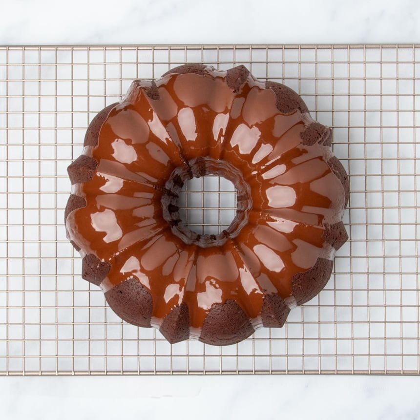 shiny wet light brown chocolate glaze poured on top of baked overturned bundt cake on wire rack