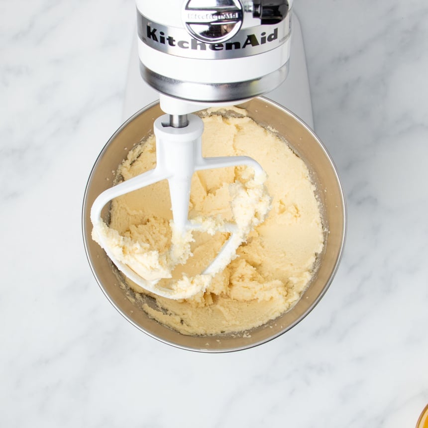 white kitchenaid stand mixer with tilt head tilted up with white paddle attachment with plate yellow whipped butter and sugar