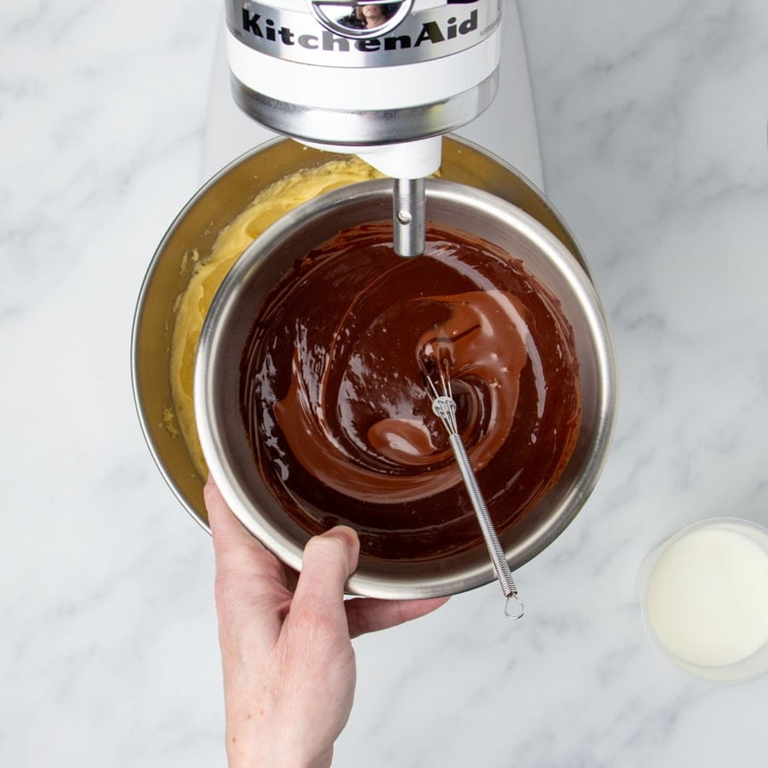 hand holding small round metal mixing bowl with soft dark chocolate mixture with very small wire whisk