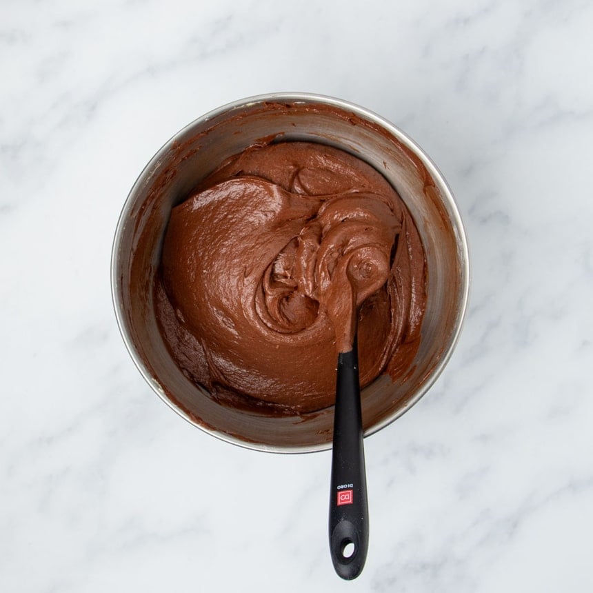 fully mixed raw brown soft cake batter with black spatula in bowl