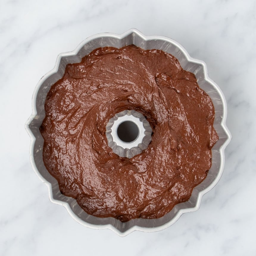 raw brown soft cake batter in classic silver cast aluminum bundt pan on marble surface