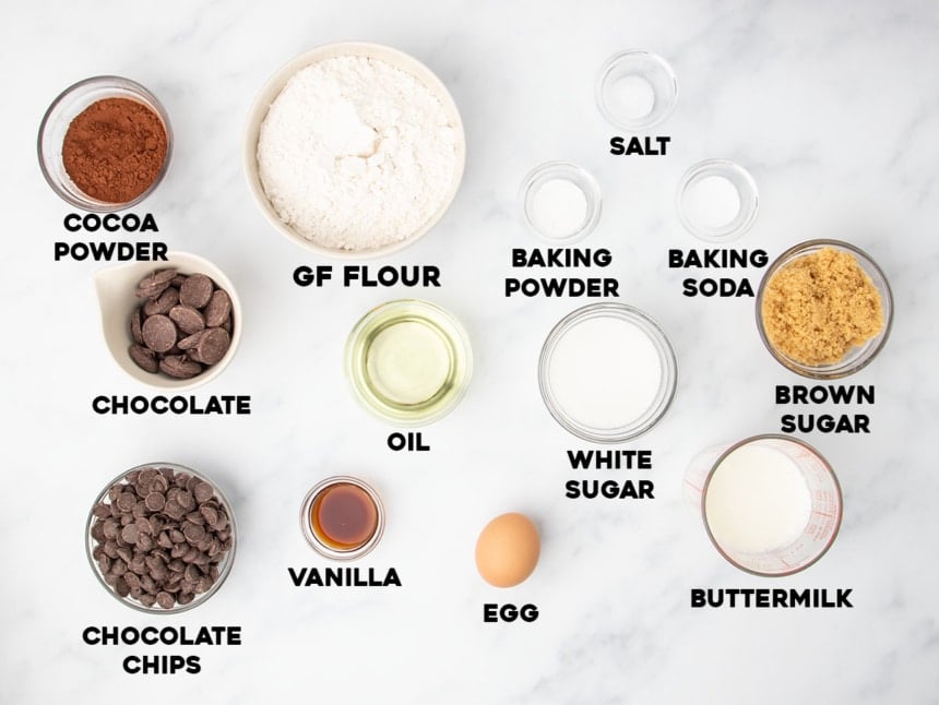 Ingredients for gluten free chocolate muffins in glass bowls on marble surface with names of ingredients in black bold type