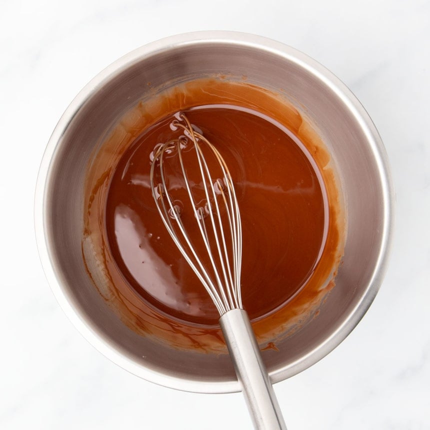 Same metal mixing bowl with oil whisked into the chocolate with a large metal wire whisk