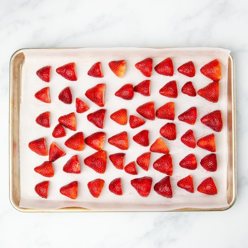 half fresh red strawberries cut side down on white paper on half metal rimmed baking sheet pan