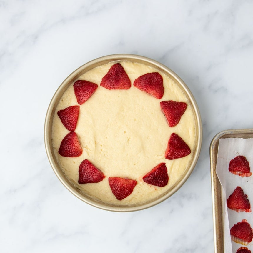 round gold metal 9-inch baking pan with yellow cake batter in single smooth layer with 1 row of cut baked strawberries around perimeter