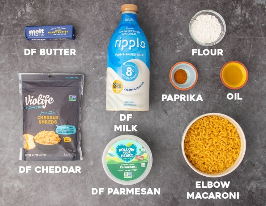 ingredients for dairy free mac and cheese in packages and small bowls with white block letters spelling out names of each ingredient