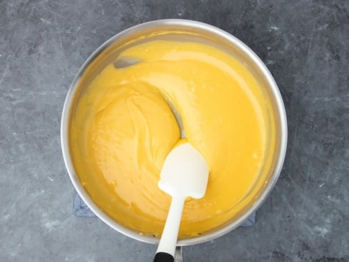 white silicone spatula stirring thick orange cheese sauce in saucepan