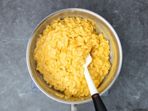 cooked elbow macaroni mixed into same cheese sauce in same pan being mixed by white spatula with black handle