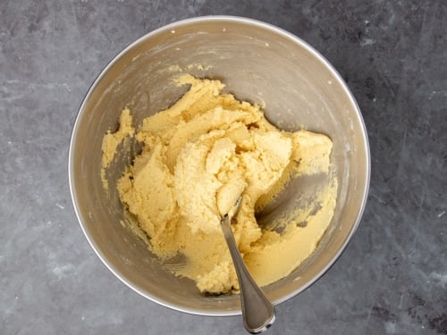 light brown stiff cookie dough in metal mixing bowl with large metal mixing spoon