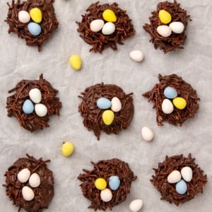 9 brown bird's nest cookies with 3 pastel-colored Cadbury mini eggs on top of each on white paper