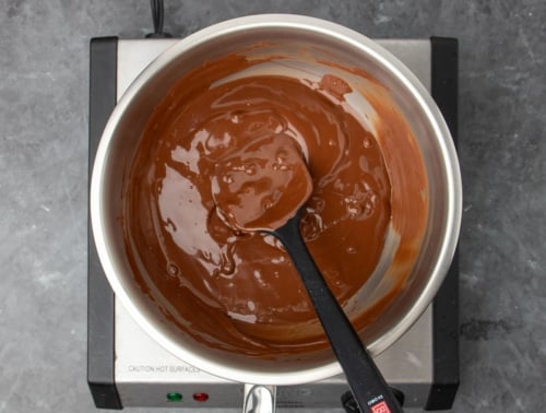 same metal mixing bowl with black silicone spatula with most of mixture melted into a brown liquid with some lumps