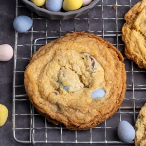 overhead image of golden brown cookie with blue mini egg candies peeking out of top on wire rack