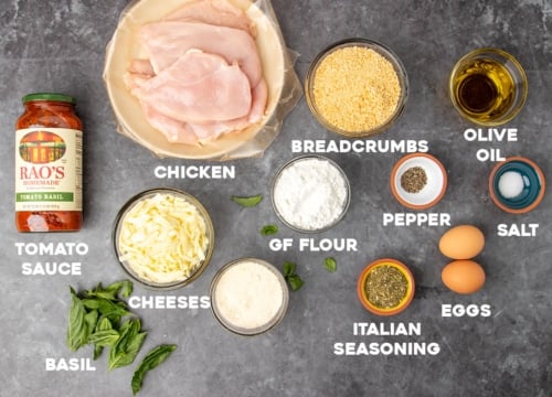 ingredients for gluten free chicken parmesan in small bowls with white block letters with names of ingredients