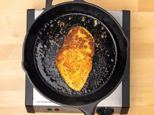 Same skillet with same cutlet browned on top side, still cooking in skillet on other side