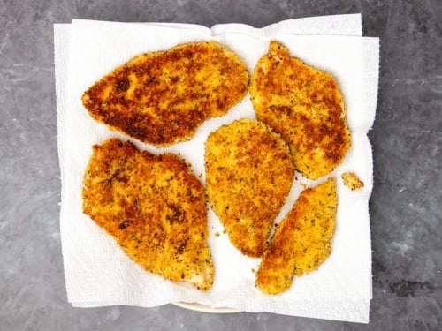 5 browned breaded chicken cutlets, some small and some large on paper towels lining dinner plate