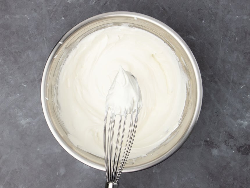 medium-size round metal bowl with white whipped cream in the bowl and some on a wire handheld whisk