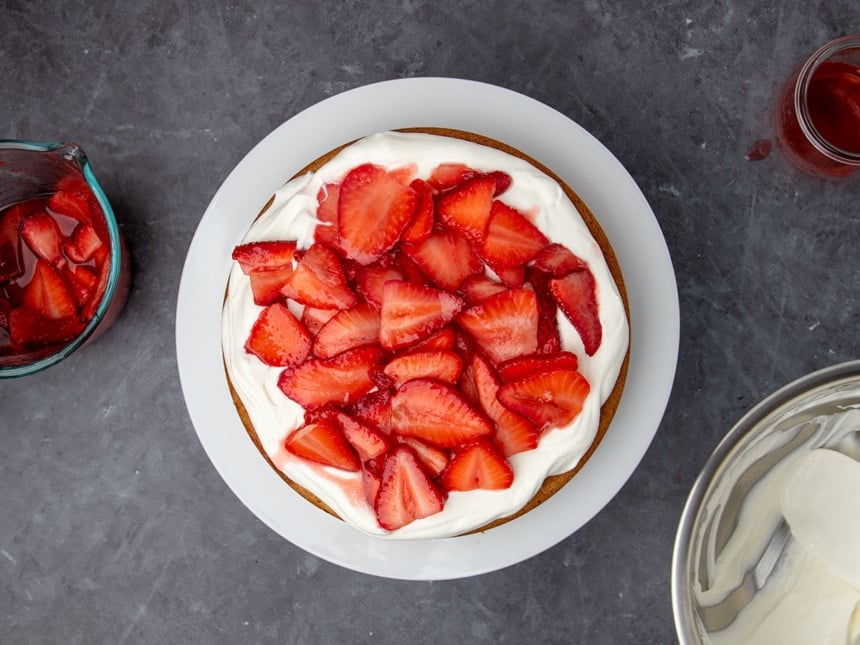 same cake with sliced strawberries on top of white whipped cream on cake