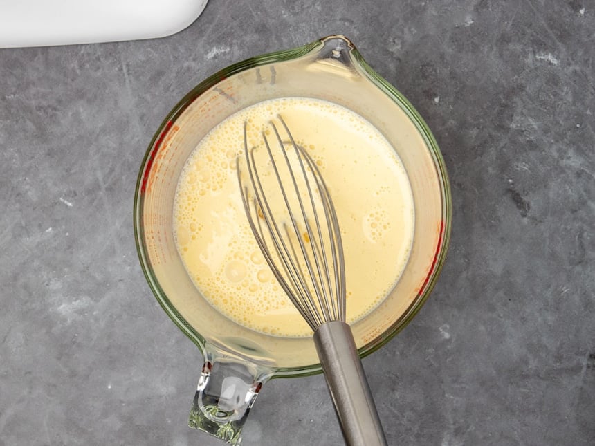 4 cup glass measuring cup with light yellow liquid and metal wire whisk