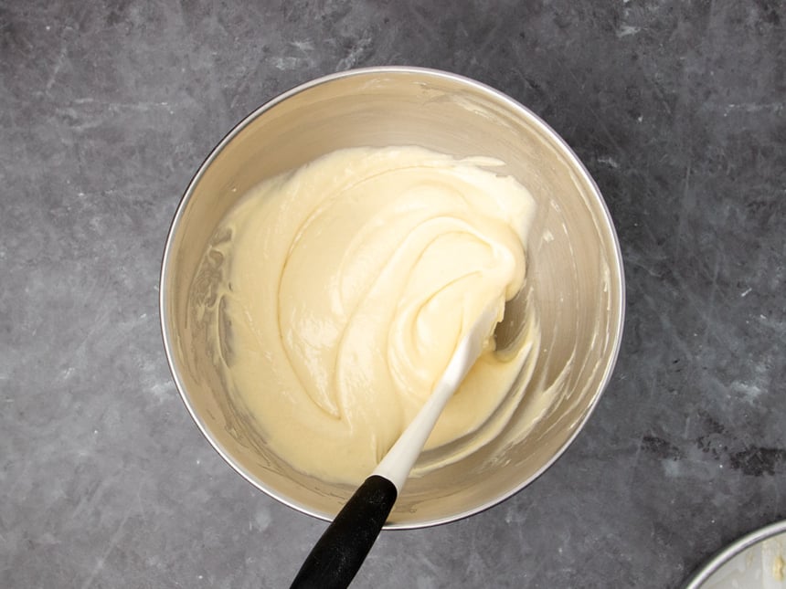 metal stand mixer bowl with soft pale yellow batter with white silicone spatula with black handle
