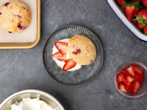 overhead image of assembled gluten free strawberry shortcake on small round dark gray plate with top of biscuit set off to the side to reveal the white whipped cream and sliced red strawberries inside