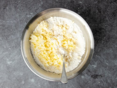 same bowl with yellow shreds of cold butter sitting on top with metal handle of mixing spoon