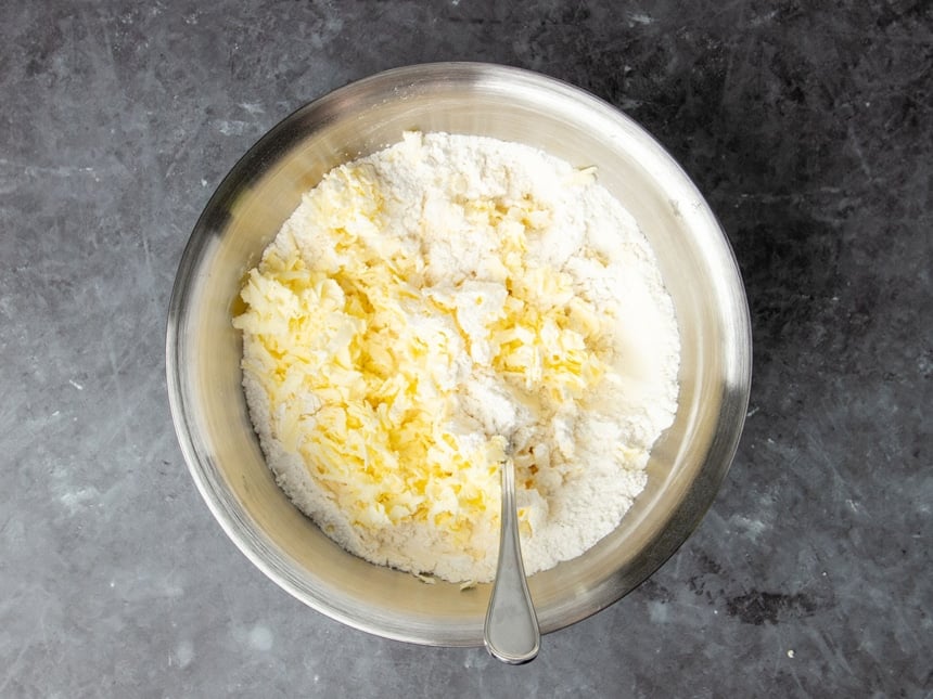 same bowl with yellow shreds of cold butter sitting on top with metal handle of mixing spoon