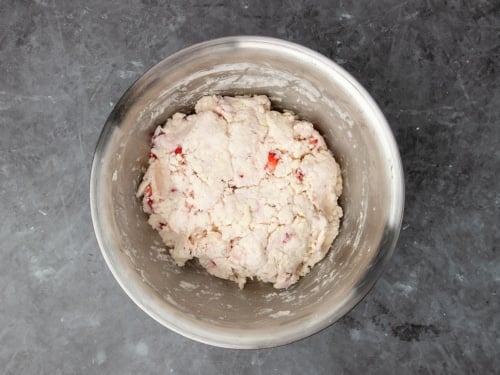 raw cream colored disk of raw biscuit dough with bright red bits of strawberries, still in mixing bowl