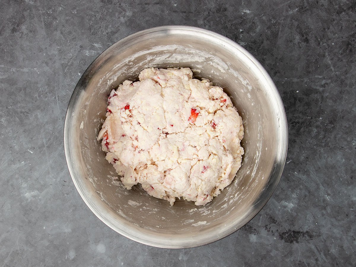 raw cream colored disk of raw biscuit dough with bright red bits of strawberries, still in mixing bowl