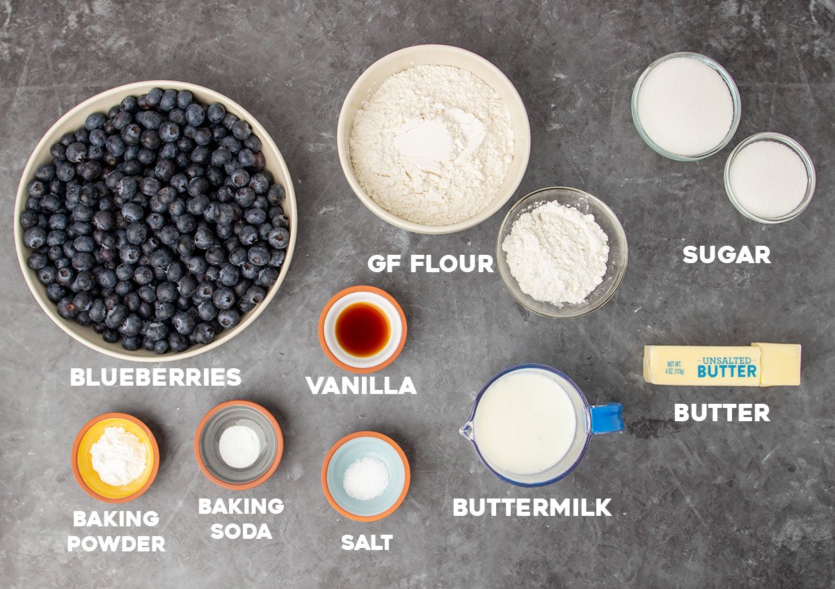 ingredients for gluten free blueberry cobbler in small bowls with white block letters spelling out names of ingredients