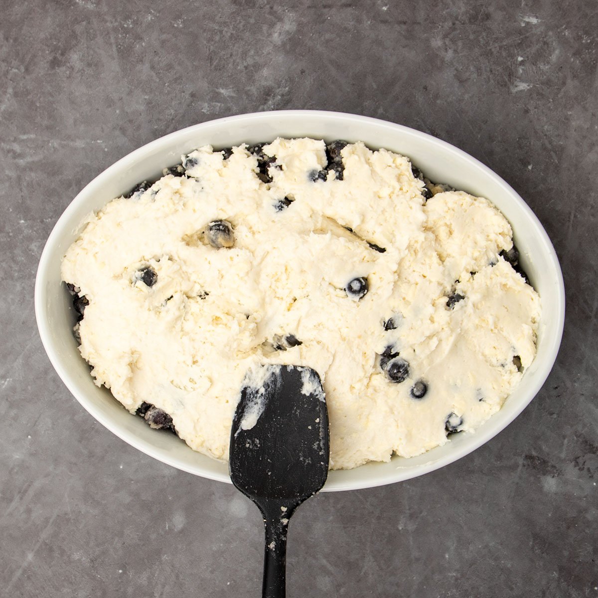 black silicone spatula on top of same dish with topping mixture spread into even layer