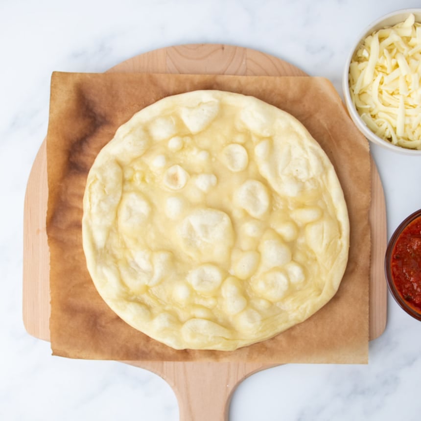 partially baked light yellow round of pizza dough with bubbles in the dough