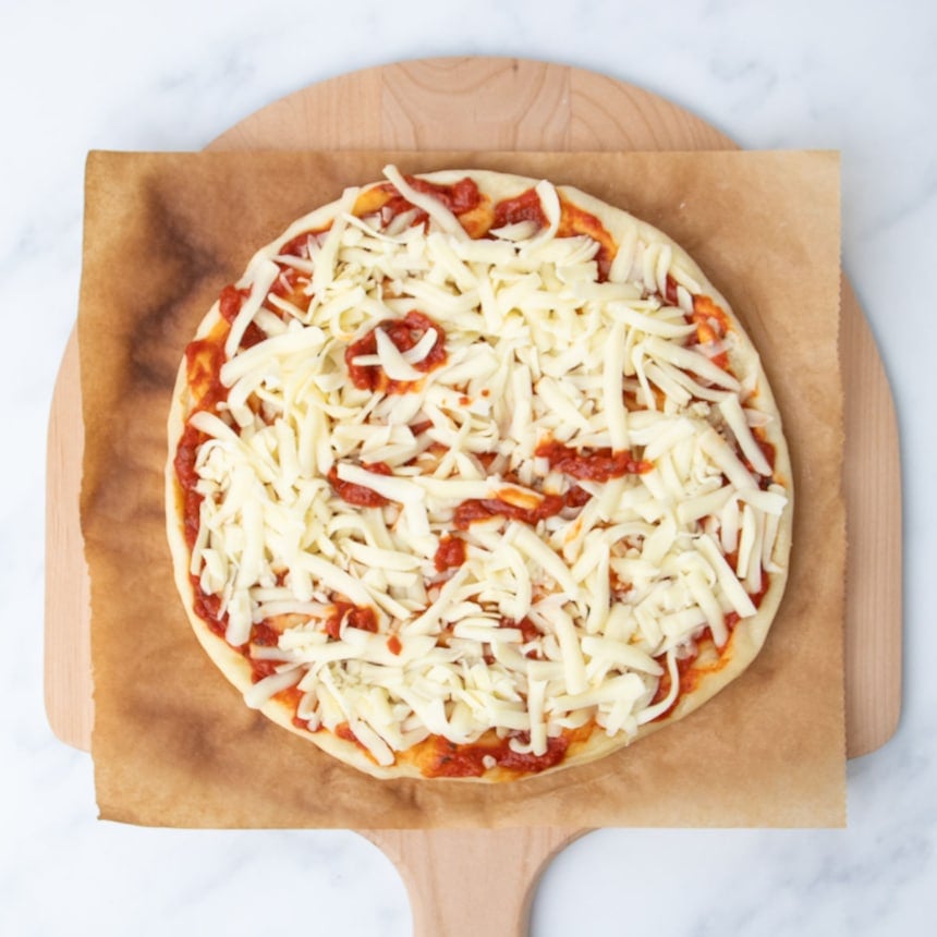 same round of parbaked pizza dough with red tomato sauce spread on top and white shreds of mozzarella cheese on top
