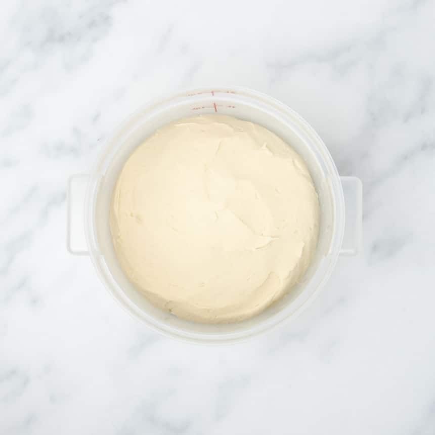 light tan raw pizza dough in a 2 quart plastic Cambro bucket
