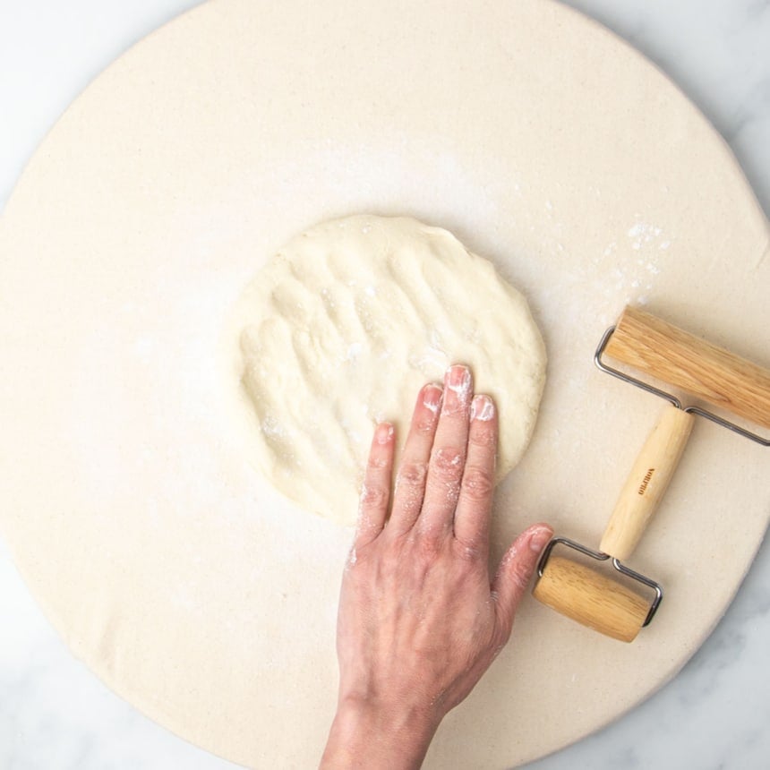 fingers of one hand pressing into raw round of pizza dough